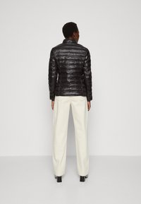 Czarna pikowana kurtka z kołnierzem, w połączeniu z kremowymi szerokimi spodniami i czarnymi botkami do kostek.