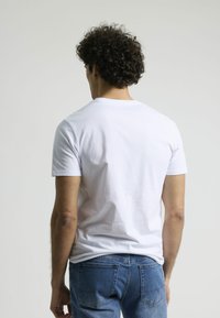 Camiseta de algodón blanca con mangas cortas, ajuste estándar y cuello redondo, combinada con jeans de mezclilla azul con bolsillos traseros.