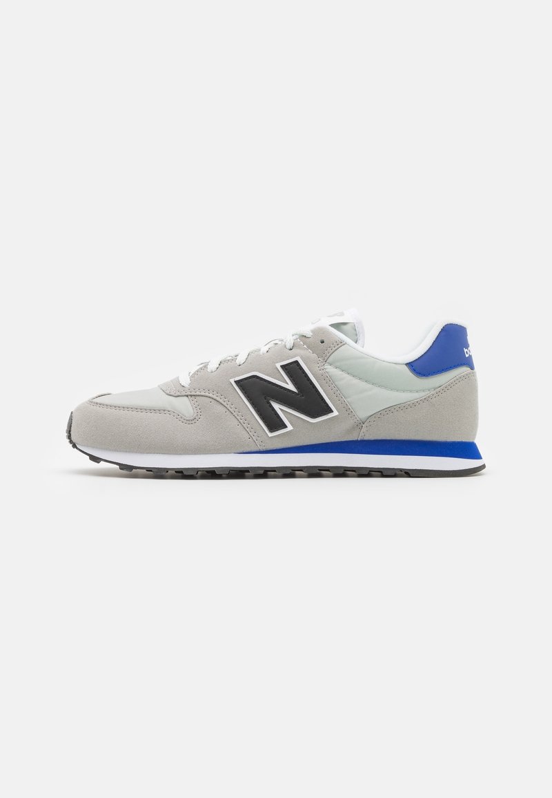 Baskets gris clair et blanc avec des accents bleus et un logo noir "N" sur le côté, montrées de profil sur fond blanc.