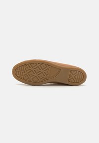 Rubber sneaker sole in light brown with a textured pattern featuring geometric shapes and distinct branding on the side.