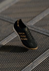 Black athletic shoe with leopard print accents, textured toe box, smooth leather, and three gold stripes. Lightweight rubber sole.