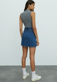 Gray ribbed sleeveless top paired with a high-waisted blue denim mini skirt, featuring a fitted design and back pockets. Worn with white socks and sneakers.