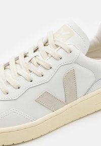 Witte leren sneaker met een beige suede V-logo, off-white veters en een getextureerde crèmekleurige rubberen zool met zichtbare stiksels.