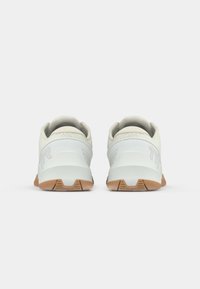 Een paar witte sportschoenen met beige zolen en gevoerde kraag gezien vanaf de achterkant op een effen lichte achtergrond.