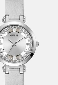 Sølv analog ur med et rundt urkasse, krystaludsmykninger og lys grå læderrem. Har en minimalistisk urskive med metalliske markører.