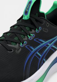 Scarpa da ginnastica nera con tomaia texturizzata, accentuazioni verdi e blu, sistema di laccio intricato e soletta ammortizzata con un design multicolore.