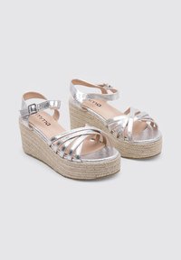 Sandalias de cuña plateadas con tiras, plataforma de yute al estilo espadrille, correa ajustable en el tobillo y textura metálica suave.