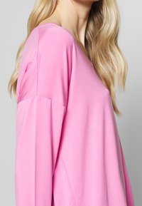 Maglietta rosa a maniche lunghe realizzata in tessuto morbido, con scollatura a V e vestibilità morbida con spalle scese per un maggiore comfort.
