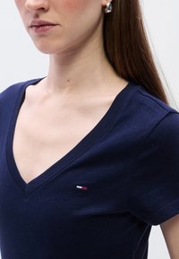 Μπλε ναυτικό V-neck μπλουζάκι από βαμβάκι, με μικρό κεντημένο λογότυπο σε κόκκινο, λευκό και μπλε στο στήθος. Λείο υφή.