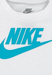 Valge T-särk sinise Nike logo ja julge tekstiga, millel on eristuv kaarjas swooshi disain. Puuvillane kangas, millel on sile tekstuur.