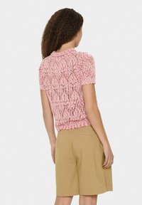 Top in pizzo rosa a maniche corte con motivo a onde, abbinato a pantaloni corti beige con tasca sul retro. Tessuto morbido e design aderente.
