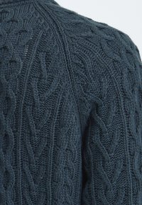 Pull tricoté bleu foncé avec des motifs complexes en torsade couvrant la surface du tissu.