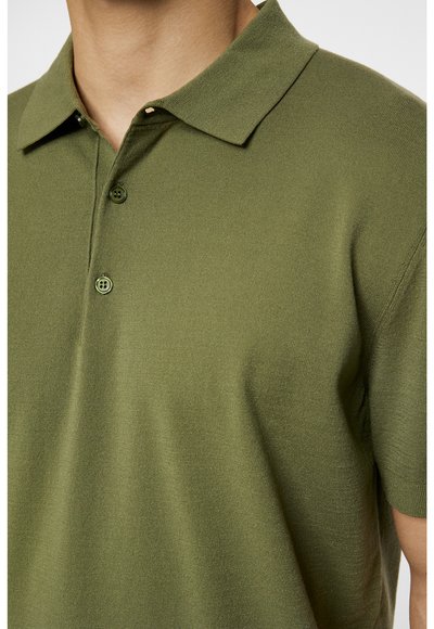 Polo vert olive en tissu doux, avec un col classique, une patte de boutonnage à trois boutons et des manches courtes avec une texture lisse.