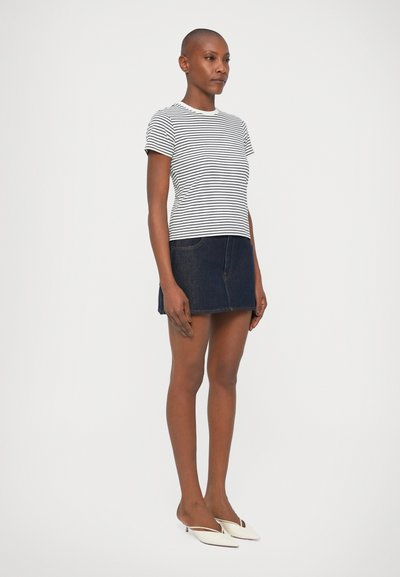 Tricou din bumbac cu dungi, cu mâneci scurte, asortat cu o fustă mini din denim. Pantofi flat albi, textură netedă și culoare bleu închis pe fustă.