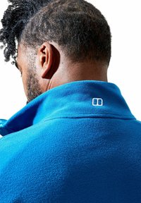 Fleecejack met hoge kraag in helderblauw, met een klein logo op de achterkant. De stof heeft een zachte, gestructureerde oppervlakte.