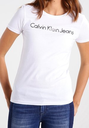 White cotton t-shirt with short sleeves, featuring "Calvin Klein Jeans" logo in black across the chest. Soft texture and crew neckline.