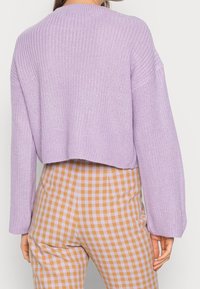 Maglione lavorato a maglia lilla con taglio corto e maniche ampie, abbinato a pantaloni a quadri gialli e viola a vita alta.