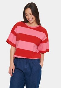 Rød og lyserød stribet t-shirt med korte ærmer, rund hals og afslappet pasform, parret med mørkeblå brede bukser.