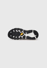 Semelle de chaussure en caoutchouc noir avec un motif de semelle texturé et multidirectionnel ; accents blancs près de la semelle intermédiaire, avec un détail de logo jaune.