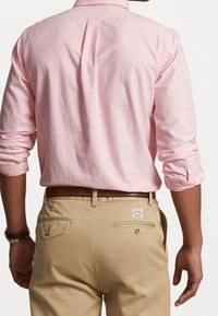 Lichtroze overhemd met lange mouwen en opgerolde manchetten, gedragen met beige chino's met achterzakken en een label op de tailleband.