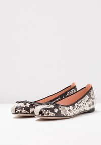 Ballet flats with a black and white snake print pattern, rounded toe, and decorative bow detail at the front. Soft leather lining.