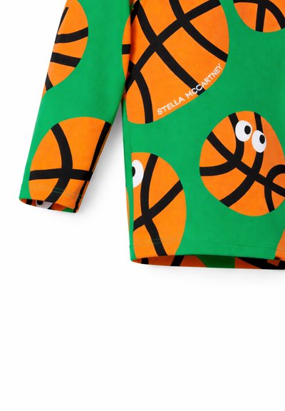 Tissu vert avec de grands ballons de basket orange ornés de lignes noires et d'yeux blancs, "Stella McCartney" imprimé sur un des ballons.