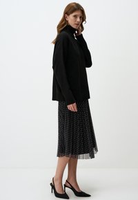 Maglione nero di grandi dimensioni con collo alto in un maglione a trama, abbinato a una gonna midi a pois. Tacchi slingback neri completano il look.