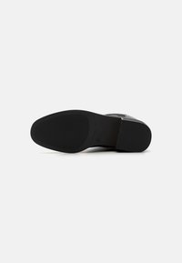 Sorte gummisåle med en teksturert overflate, glatt svart hæl og et elegant design. Har en enkel, minimalistisk form.