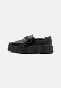 Zwarte loafers met een glanzende afwerking, voorzien van een ronde neus, geribbeld zwart zool en een band over de bovenkant voor extra detail.