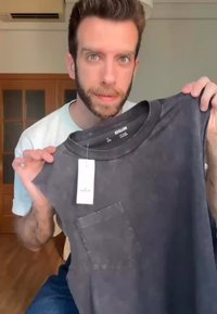 Melnas bez piedurknēm T-krekls ar apaļu kakla izgriezumu, ar krūšu kabatu un karodziņu. Audums izskatās mīksts ar nolietotu tekstūru.