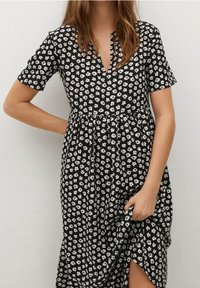 Vestido negro con mangas cortas, estampado floral blanco, escote en V, bodice ajustado y falda acampanada, con una abertura lateral y textura de tela suave.