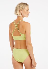 Zelený pruhovaný bikini set s kříženými popruhy na zádech, s texturovaným povrchem a středně vysokým spodním dílem. Jednoduchý design, bez vzorů či akcentů.