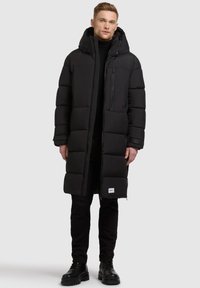 Sort, polstret vinterjakke med hætte, der har en frontlynlås og en brystlomme. Stoffet ser glat ud med en puffy, quiltet tekstur.