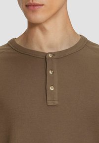 Braun gestreifte Langarmshirt mit Rundhalsausschnitt, ausgestattet mit einem dreifachen Knopfverschluss am Kragen und strukturiertem Stoff.