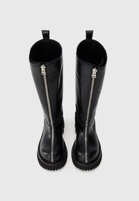 Schwarze kniehohe Stiefel mit silbernen Reißverschlüssen vorne und dicken Profilsohlen, die auf einem schlichten Hintergrund nach vorne gerichtet sind.