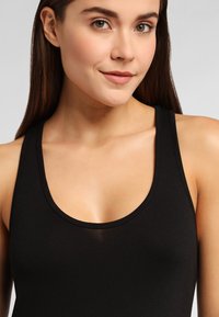 Top negro sin mangas con escote redondeado y tejido suave, que resalta un diseño ligero sin costuras ni patrones visibles.