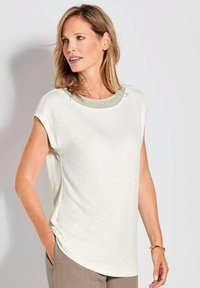 Helles weißes Kurzarmoberteil mit einem runden Ausschnitt, das mit einem Perlenakzent versehen ist. Weicher Stoff mit legerem Schnitt und einem abgerundeten Saumdesign.