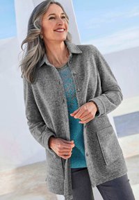 Grau Fleece-Knopfjacke mit Kragen, Fronttasche und strukturiertem Stoff, über einem blauen Strickoberteil getragen, kombiniert mit dunklen Hosen.