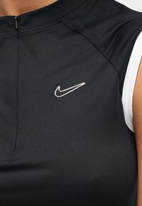 Top deportivo negro con mangas cortas blancas, cremallera frontal y pequeño logo plateado de Nike en el pecho. Hecho de material ajustado y liso.
