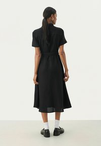 Vestito nero con cintura, maniche corte, tessuto leggero, lunghezza media, con silhouette dritta e texture sottile, mostrato da dietro.