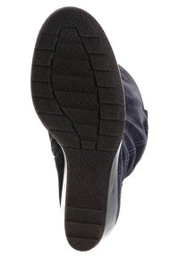 Suela de zapato de goma negra con surcos y estrías texturizadas, que presenta una impresión de logotipo circular. La parte superior parece oscura, posiblemente de tela o ante.