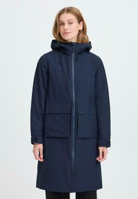 Temno modra dežna jakna s kapuco, sprednjim zadrgo in dvema velikima sprednjima žepoma. Ima sproščen kroj in teksturirano tkanino za dodatno vzdržljivost.