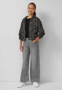 Bomberjacke mit Leopardenmuster in Grau und Schwarz, kombiniert mit grauen weit geschnittenen Jeans und weißen Sneakern. Glatte Textur, lässige Passform.