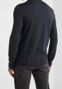 Långärmad marinblå skjorta i ett mjukt, slätt tyg med rund halsringning och en avslappnad passform, parat med mörkgrå jeans.