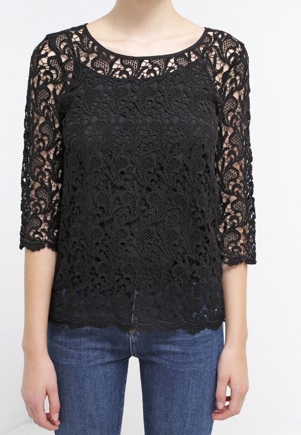 Top in pizzo nero con maniche a tre quarti, caratterizzato da intricate fantasie floreali, scollatura rotonda e orlo scallop. Indossato sopra jeans blu.