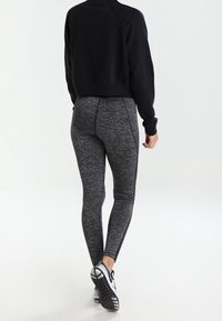 Felpa nera corta e leggings grigi con motivo e strisce nere sui lati. Un piede in una sneaker con suola texturizzata.
