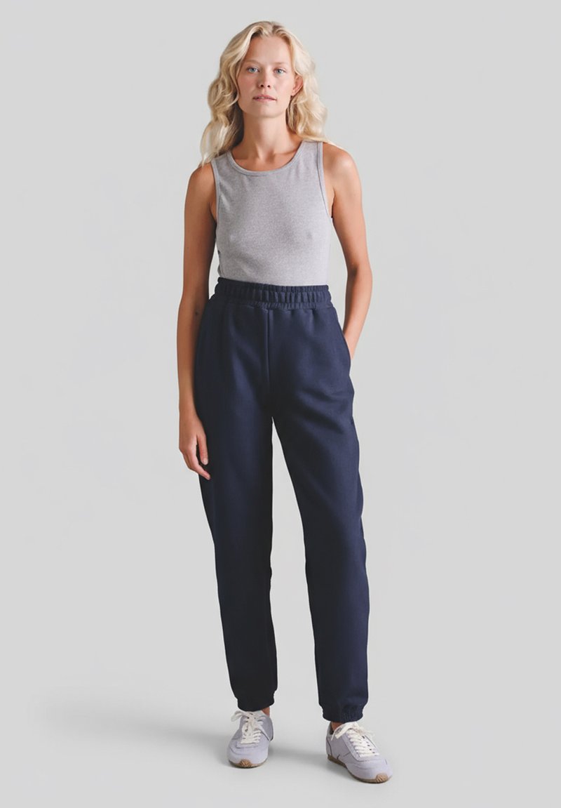 Szary bezrękawnik i granatowe spodnie dresowe z elastycznym paskiem w talii, zwężane przy kostkach. Model nosi jasnoszare trampki.