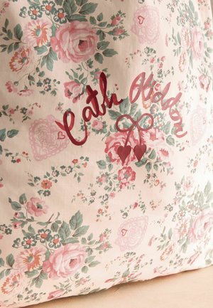 Blomstret stof med pink roser og grønne blade, med kursiv rød tekst og to hængende hjerteformer i midten.