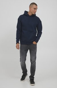 Navy blue hoodie with a front pocket and a drawstring hood, paired with gray jeans and black sneakers, featuring a relaxed fit.