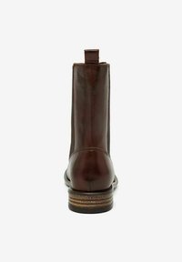 Bottine en cuir brun à bout rond, de forme slim et à petit talon empilé. Elle présente une languette à l'arrière et une texture lisse.